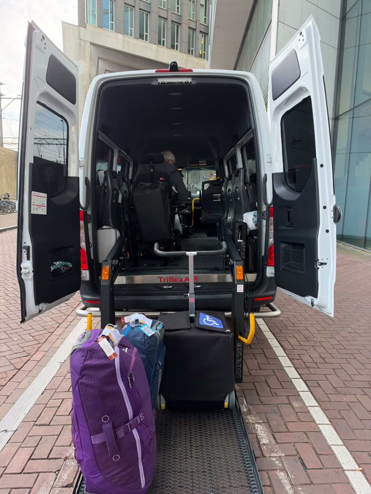 Rolstoelbus met bagage op de laadklep en een reiziger in een elektrische rolstoel