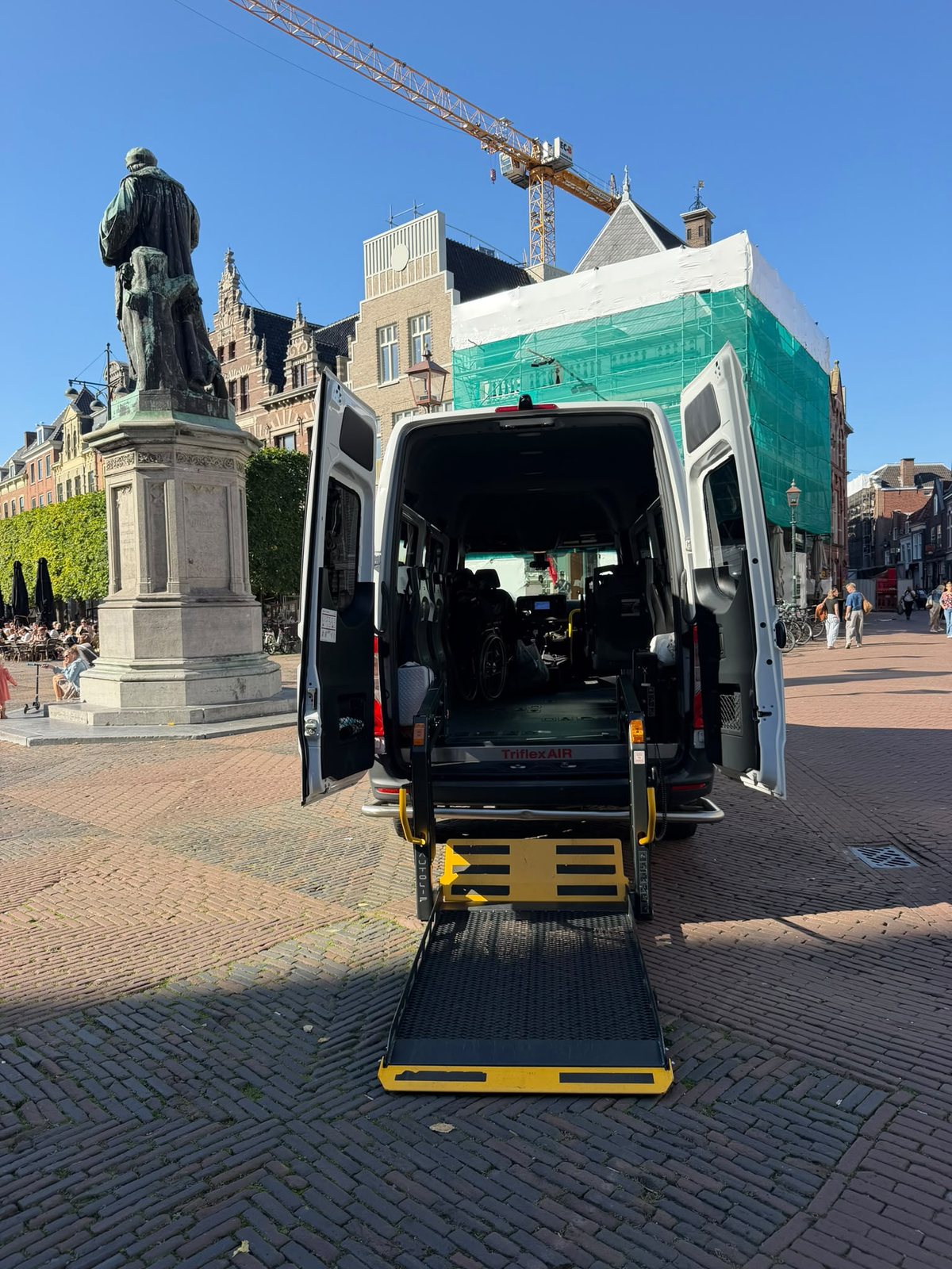 Rolstoelbus met uitgeklapte laadklep op de Grote Markt in Haarlem, naast het standbeeld van Laurens Janszoon Coster