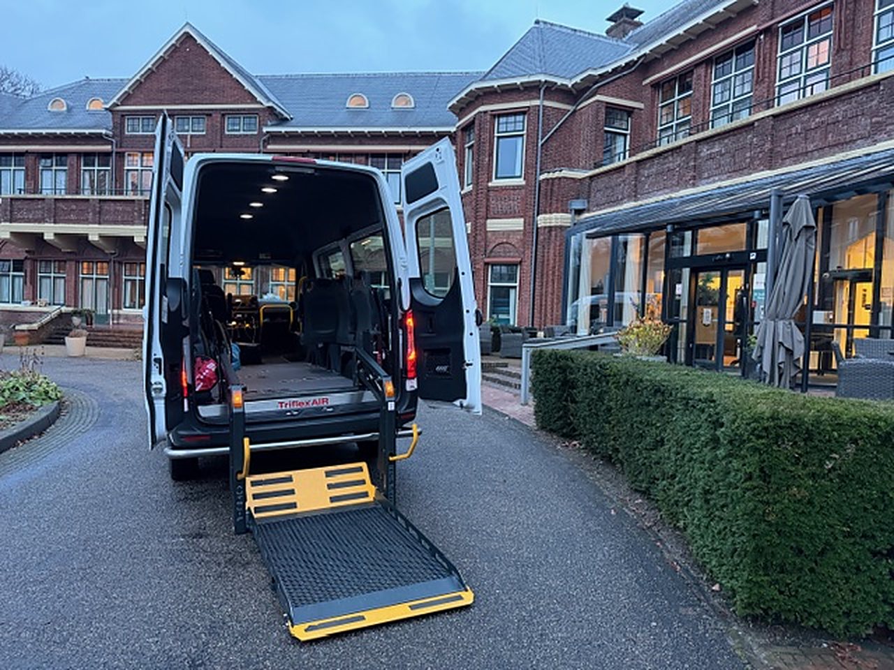 Rolstoelbus met laadklep voor een gebouw van rode baksteen