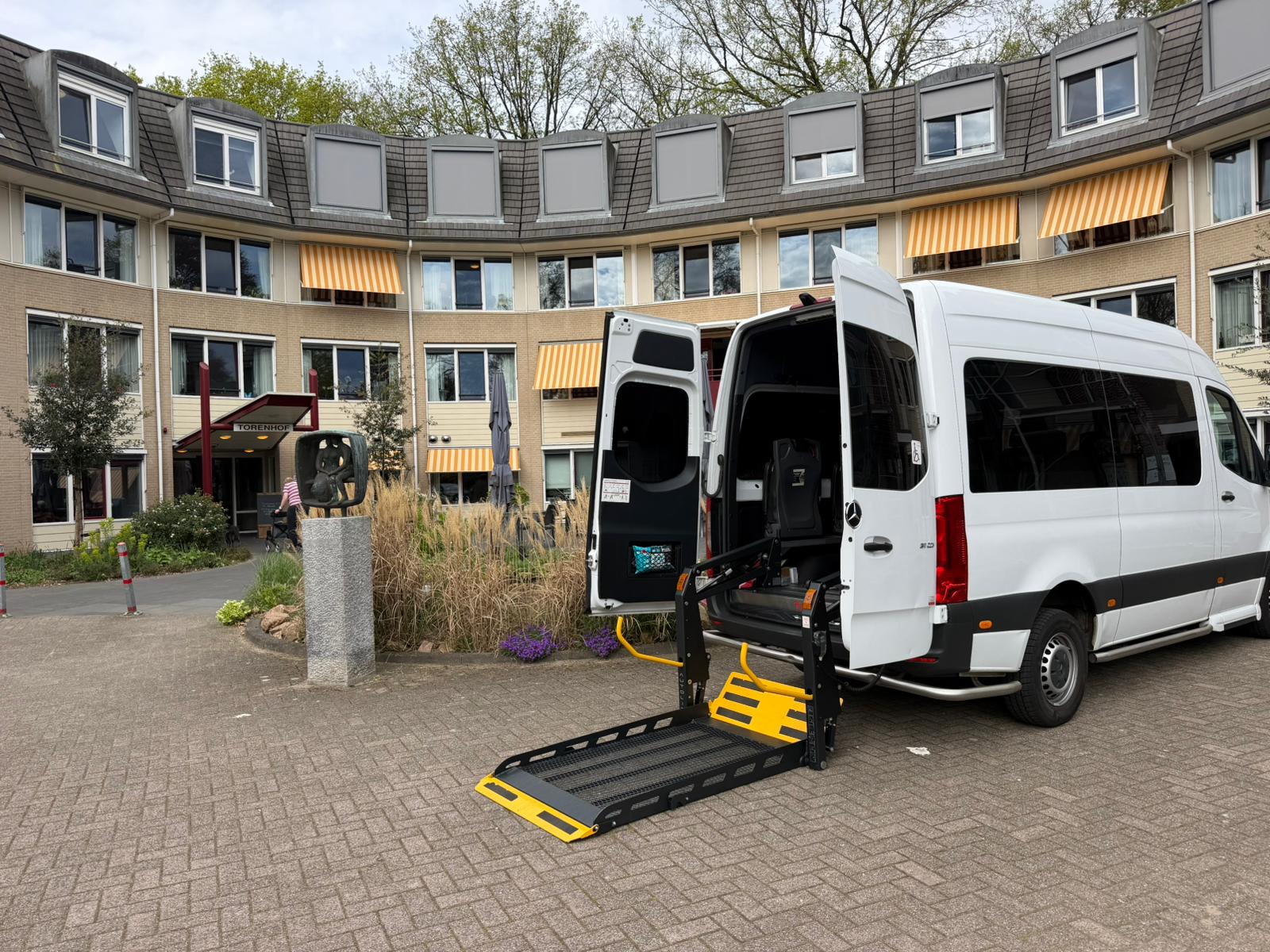 Rolstoelbus met laadklep bij de ingang van een zorginstelling